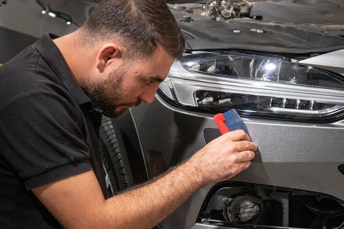 Professional installer applying vinyl wrap to a car bumper using a squeegee in a climate-controlled shop