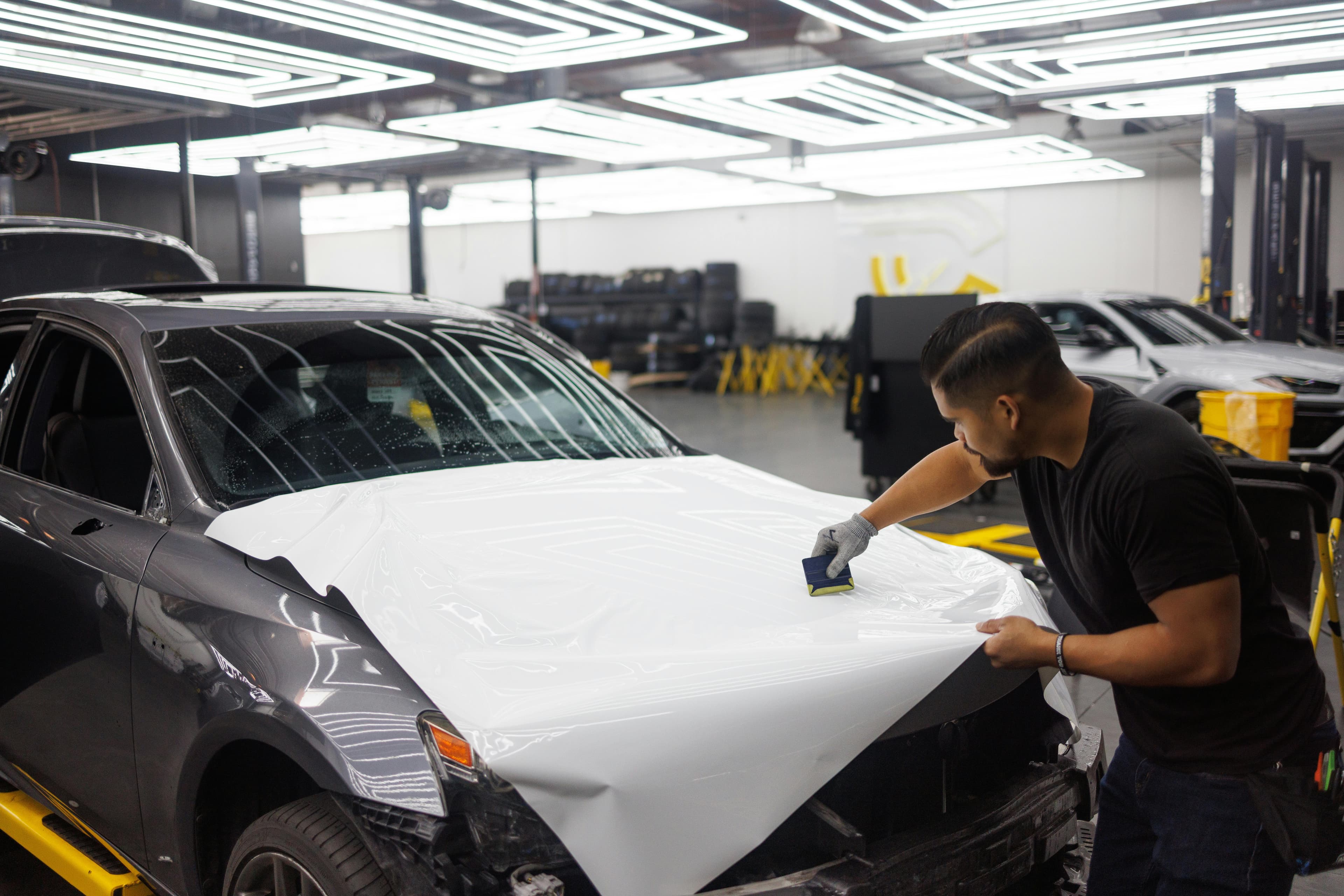 Professional installer applying white vinyl wrap to a car hood in a climate-controlled shop