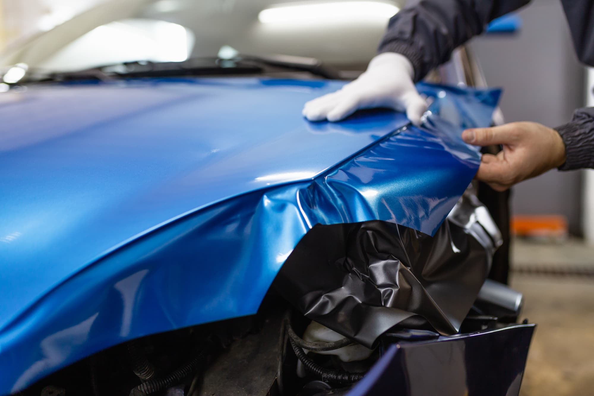 Professional installer applying blue vinyl wrap to a car fender, demonstrating precision car wrap installation technique